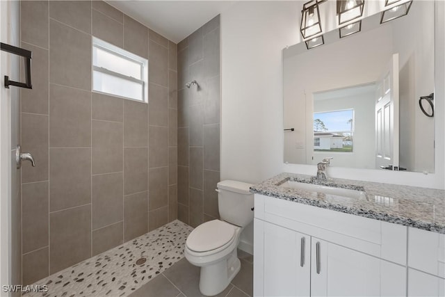 bathroom with toilet, tiled shower, tile patterned flooring, and vanity