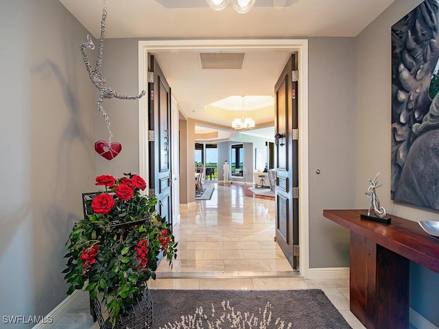 5051 Pelican Colony Blvd Unit 301, Bonita Springs, FL 34134 - hallway featuring a tray ceiling, baseboards, light tile patterned flooring, and a chandelier