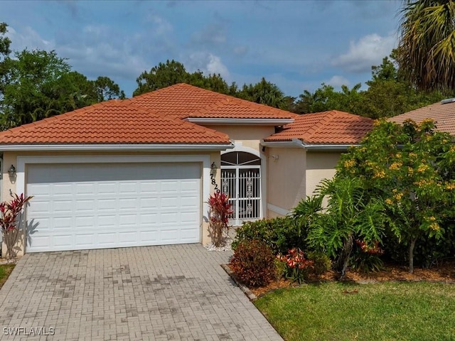 mediterranean / spanish home with stucco siding, decorative driveway, a tiled roof, and an attached garage