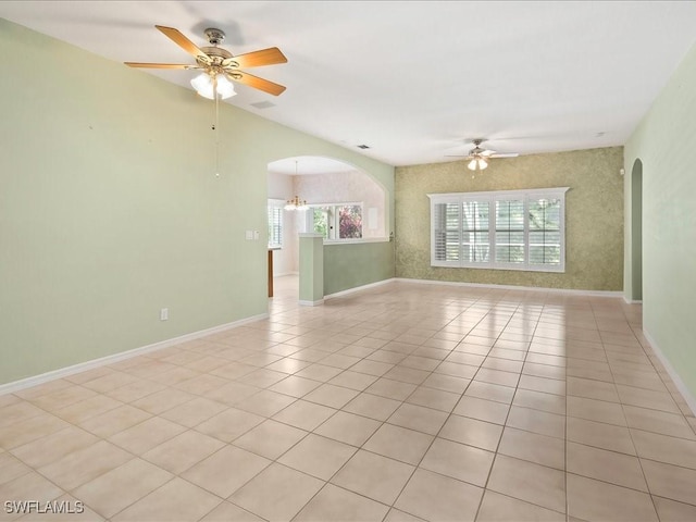 empty room with a wealth of natural light, arched walkways, and ceiling fan with notable chandelier
