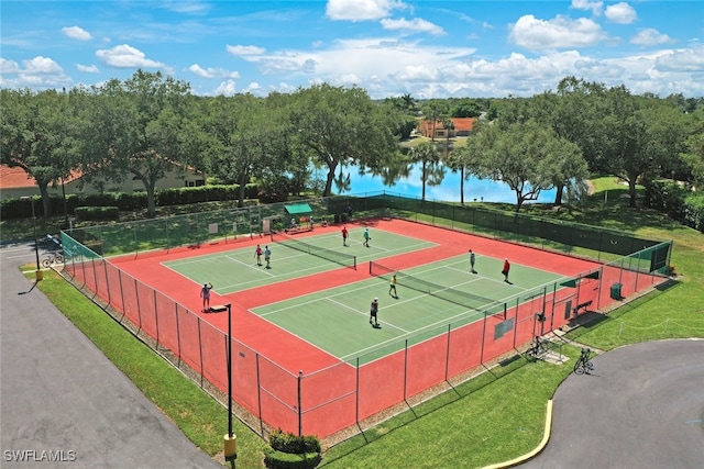 view of tennis court with a lawn, a water view, and fence