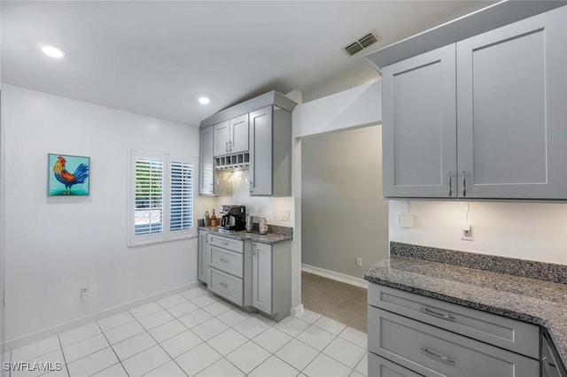 kitchen featuring dark stone counters, baseboards, visible vents, and gray cabinets