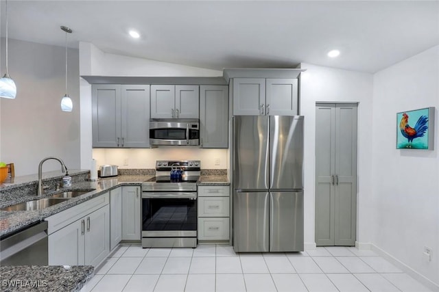 kitchen with appliances with stainless steel finishes, a sink, lofted ceiling, dark stone counters, and light tile patterned flooring