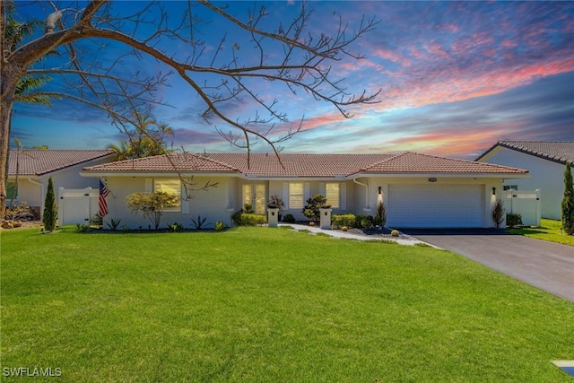view of front of home featuring aphalt driveway, fence, an attached garage, a tile roof, and a front lawn
