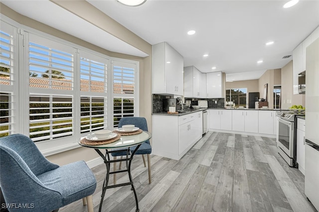 13471 Bridgeford Ave, Bonita Springs, FL 34135 - kitchen with white cabinets, stainless steel electric range oven, light wood finished floors, dark countertops, and backsplash