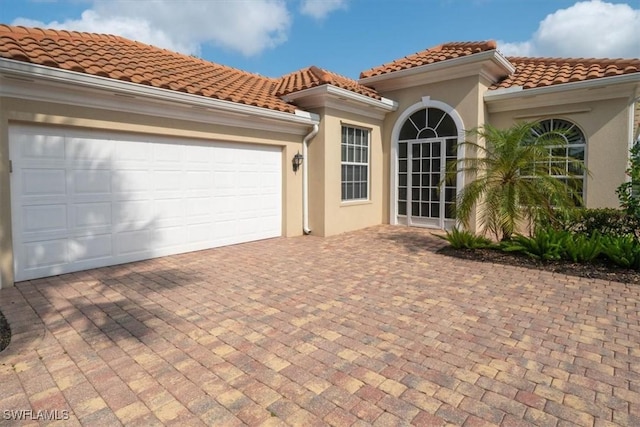 view of front of house featuring stucco siding, a tile roof, a garage, and decorative driveway