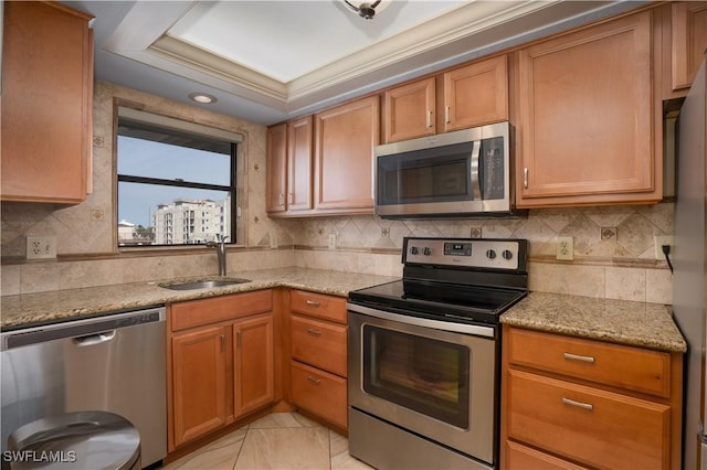 kitchen with light stone counters, a sink, appliances with stainless steel finishes, brown cabinetry, and decorative backsplash