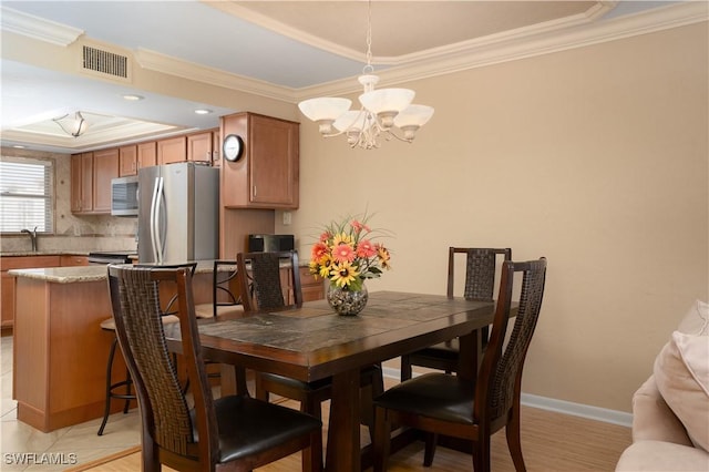 dining room featuring a notable chandelier, a raised ceiling, baseboards, visible vents, and ornamental molding