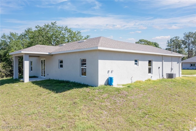 rear view of property featuring central air condition unit, stucco siding, and a yard