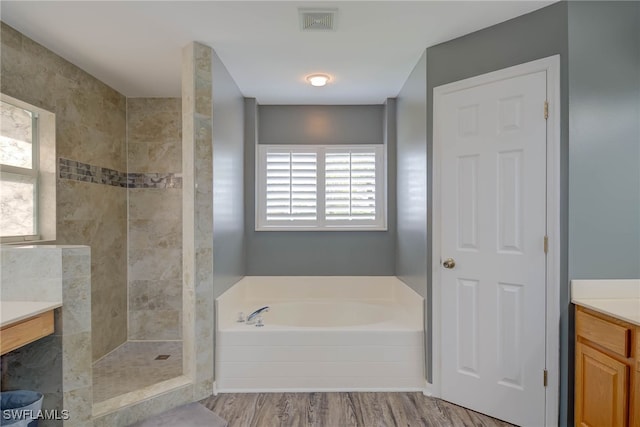 bathroom with a bath, visible vents, wood finished floors, vanity, and tiled shower