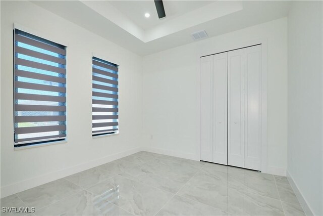 unfurnished bedroom featuring marble finish floor, a tray ceiling, baseboards, visible vents, and recessed lighting