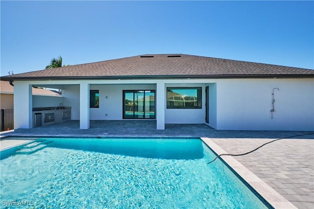 rear view of house featuring a patio area, an outdoor kitchen, an outdoor pool, and stucco siding