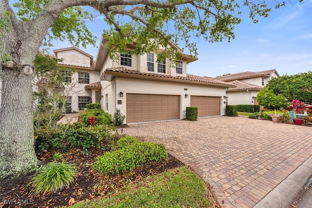 mediterranean / spanish home with decorative driveway, a tile roof, stucco siding, and an attached garage