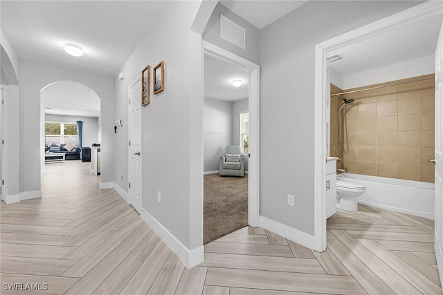 corridor featuring arched walkways, visible vents, and baseboards