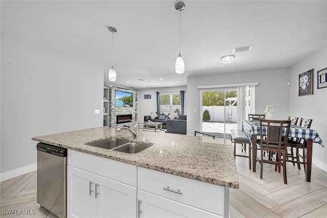 kitchen with dishwasher, a fireplace, a center island with sink, a sink, and open floor plan