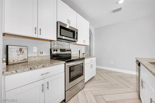kitchen featuring stainless steel appliances, baseboards, light stone counters, visible vents, and white cabinets