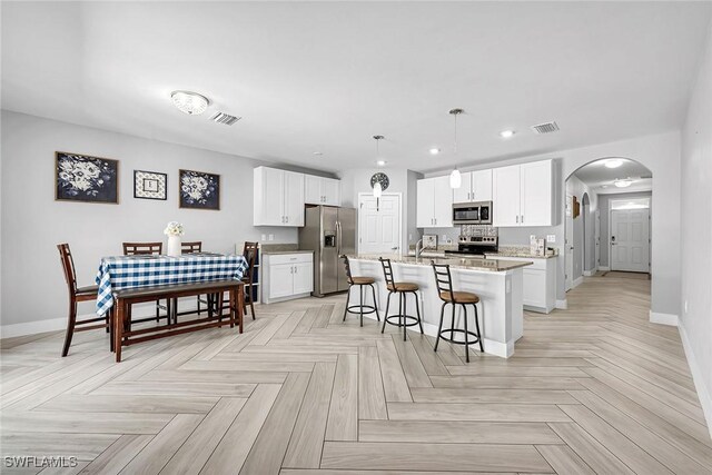 kitchen with a kitchen bar, stainless steel appliances, arched walkways, visible vents, and white cabinets