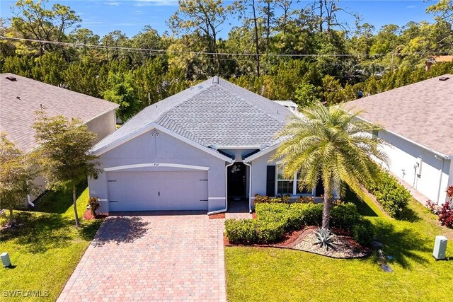 view of front facade with a front yard, stucco siding, an attached garage, a shingled roof, and decorative driveway