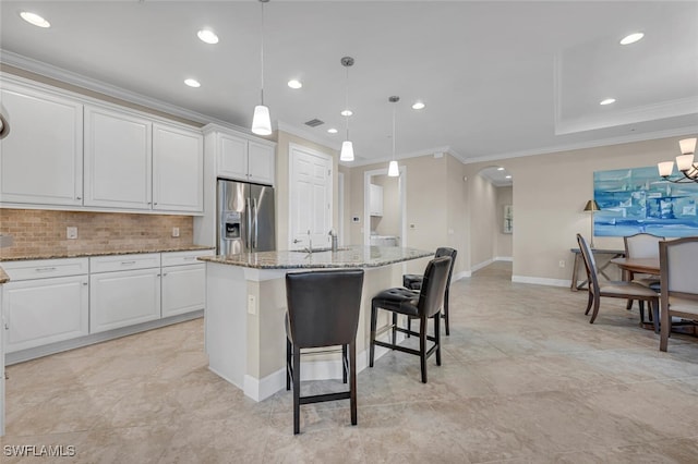 kitchen featuring stainless steel fridge, a kitchen island with sink, light stone countertops, arched walkways, and a sink