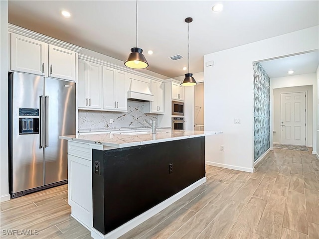 kitchen with an island with sink, premium range hood, stainless steel appliances, light wood-style flooring, and decorative backsplash