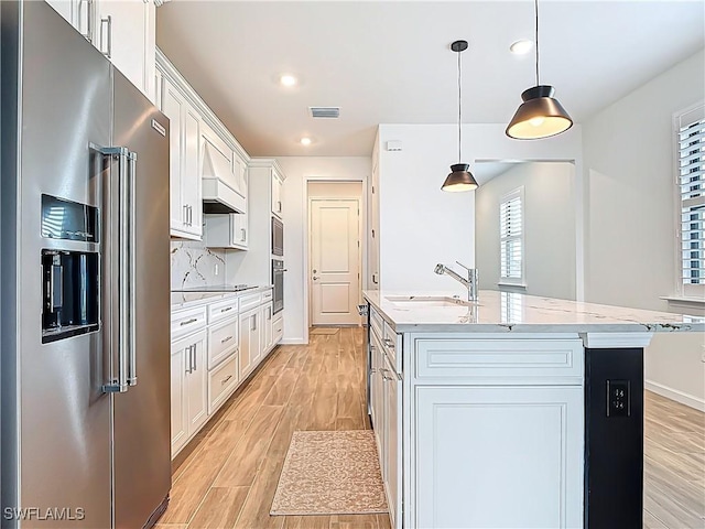 kitchen featuring white cabinets, a kitchen island with sink, appliances with stainless steel finishes, light wood finished floors, and a sink