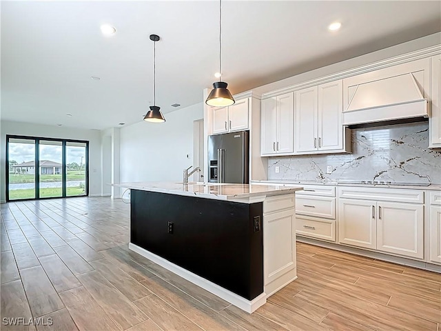 kitchen with high end refrigerator, a kitchen island with sink, backsplash, and white electric cooktop