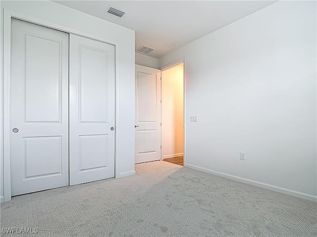 unfurnished bedroom featuring light carpet, a closet, baseboards, and visible vents