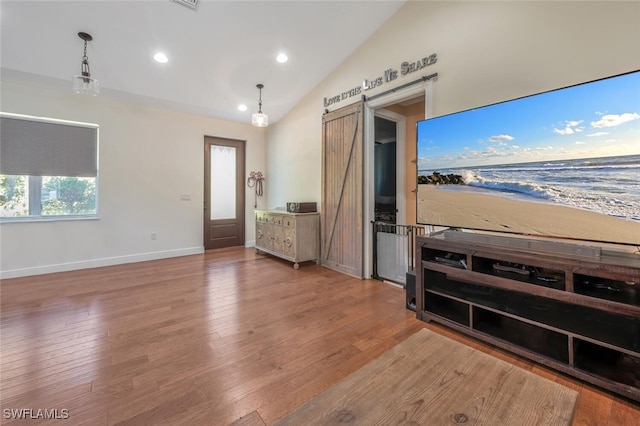 unfurnished living room with a barn door, recessed lighting, baseboards, wood finished floors, and lofted ceiling