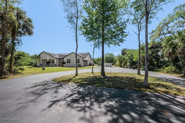 view of front of house with roof mounted solar panels, curved driveway, and a front lawn