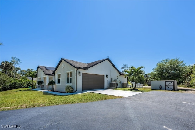 view of property exterior with an attached garage, a storage unit, a lawn, driveway, and solar panels