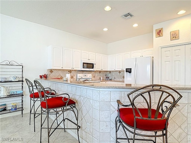 20716 Tisbury Ln, North Fort Myers, FL 33917 - kitchen with white appliances, white cabinetry, visible vents, a breakfast bar, and backsplash