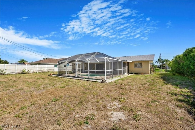 rear view of house with a lanai, fence, a yard, and an outdoor pool