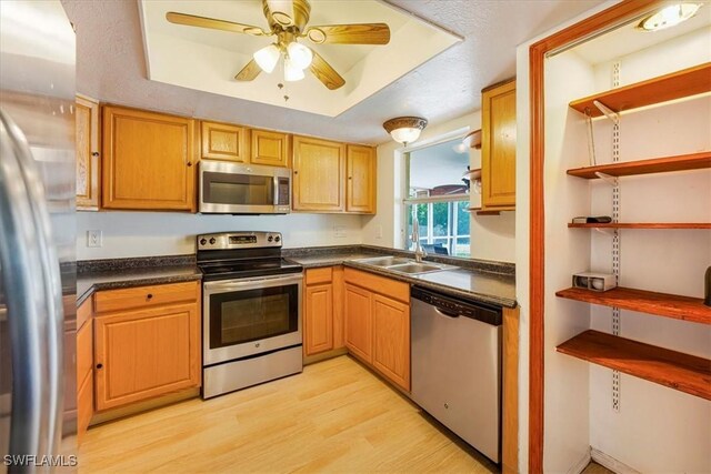 kitchen with dark countertops, a sink, stainless steel appliances, and light wood-type flooring