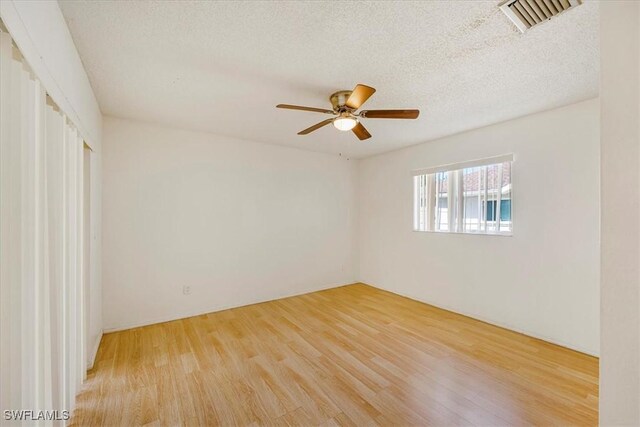 empty room with a textured ceiling, wood finished floors, ceiling fan, and visible vents