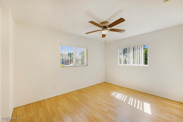 empty room with wood finished floors, a healthy amount of sunlight, ceiling fan, and baseboards