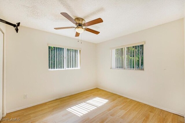 unfurnished room with a textured ceiling, a wealth of natural light, wood finished floors, and baseboards