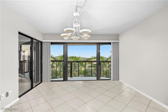 845 Collier Ct Unit 503, Marco Island, FL 34145 - spare room featuring a chandelier, healthy amount of natural light, a textured ceiling, baseboards, and light tile patterned floors