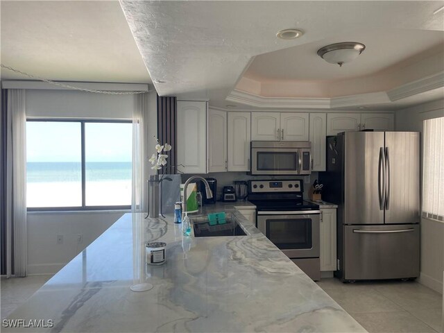 6672 Estero Blvd Unit A606, Fort Myers Beach, FL 33931 - kitchen featuring appliances with stainless steel finishes, a sink, light stone counters, a raised ceiling, and a water view