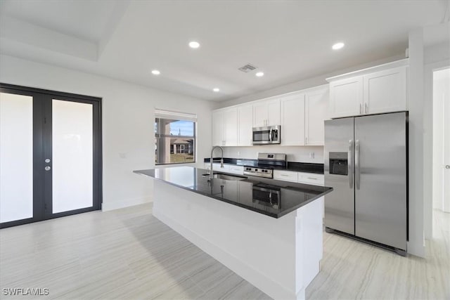kitchen featuring an island with sink, a sink, stainless steel appliances, visible vents, and white cabinets