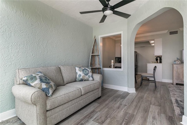 living room featuring arched walkways, ceiling fan, a textured wall, and visible vents