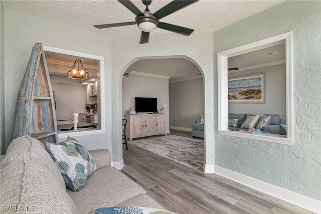 living area with baseboards, a textured wall, arched walkways, ceiling fan with notable chandelier, and wood finished floors
