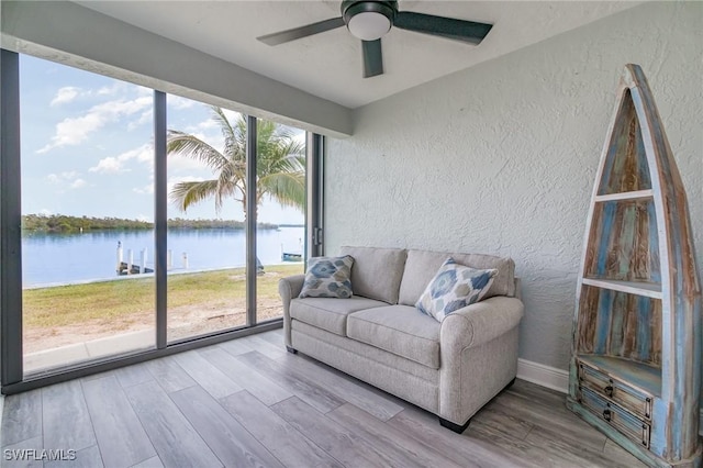 interior space with baseboards, a water view, a ceiling fan, a textured wall, and wood finished floors
