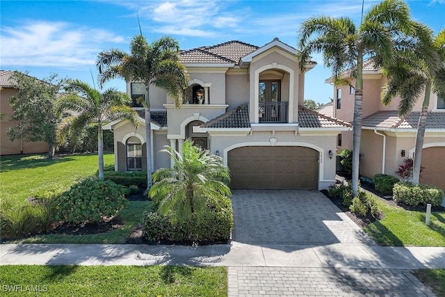 mediterranean / spanish home with a balcony, a tiled roof, stucco siding, decorative driveway, and a front lawn