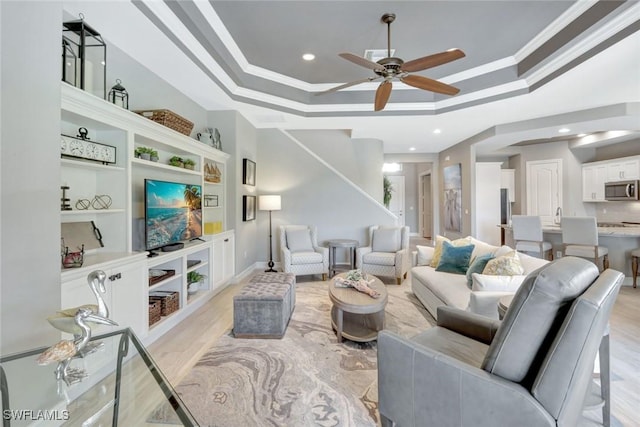 living area with a tray ceiling, ceiling fan, ornamental molding, light wood-type flooring, and recessed lighting