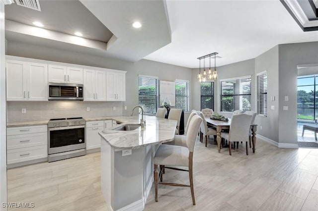 kitchen featuring stainless steel appliances, a sink, white cabinets, tasteful backsplash, and a chandelier