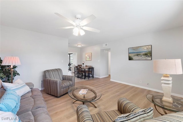 living room featuring visible vents, light wood-style flooring, a ceiling fan, and baseboards