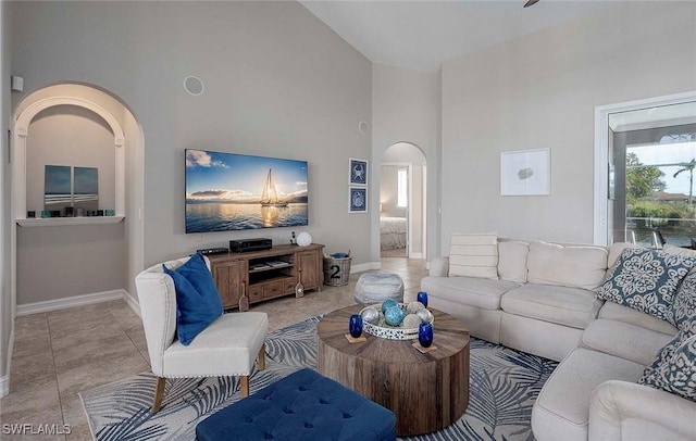 living area with baseboards, high vaulted ceiling, arched walkways, and light tile patterned floors