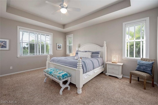 bedroom with baseboards, light colored carpet, multiple windows, and a raised ceiling