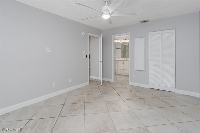 unfurnished bedroom featuring baseboards, light tile patterned flooring, ensuite bath, ceiling fan, and a closet