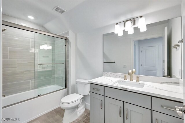 bathroom with toilet, vanity, wood tiled floor, visible vents, and shower / bath combination with glass door